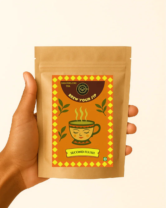 Hand holding Second flush Darjeeling loose tea leaves in a brown tea packaging with a decorative label on a beige background